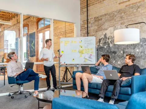 Three people working on laptops while a colleague presents at a whiteboard