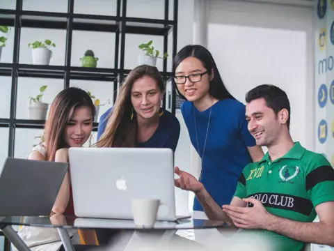 Four people gathered around a laptop on a glass table during a discussion