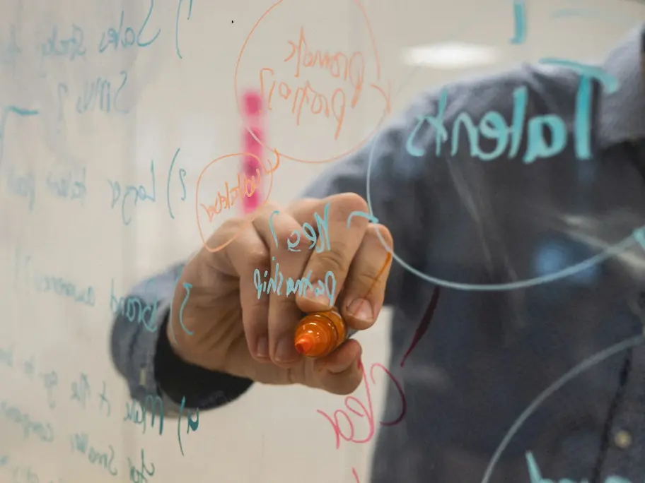 Person writing diagrams and notes on a glass whiteboard
