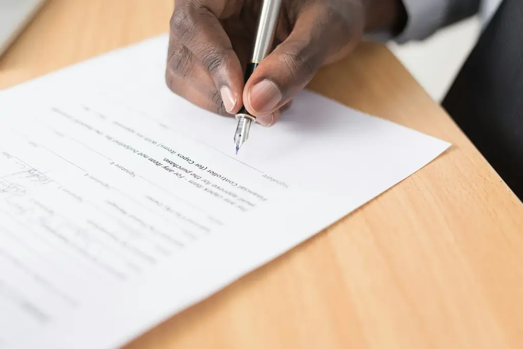 Person's hand writing on a printed document with a pen